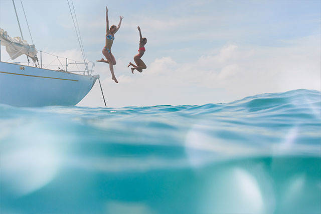 Tjejer hoppar i vattnet från segelbåt - Betala din resa till den grekiska ö-världen med ett kreditkort från re:member.